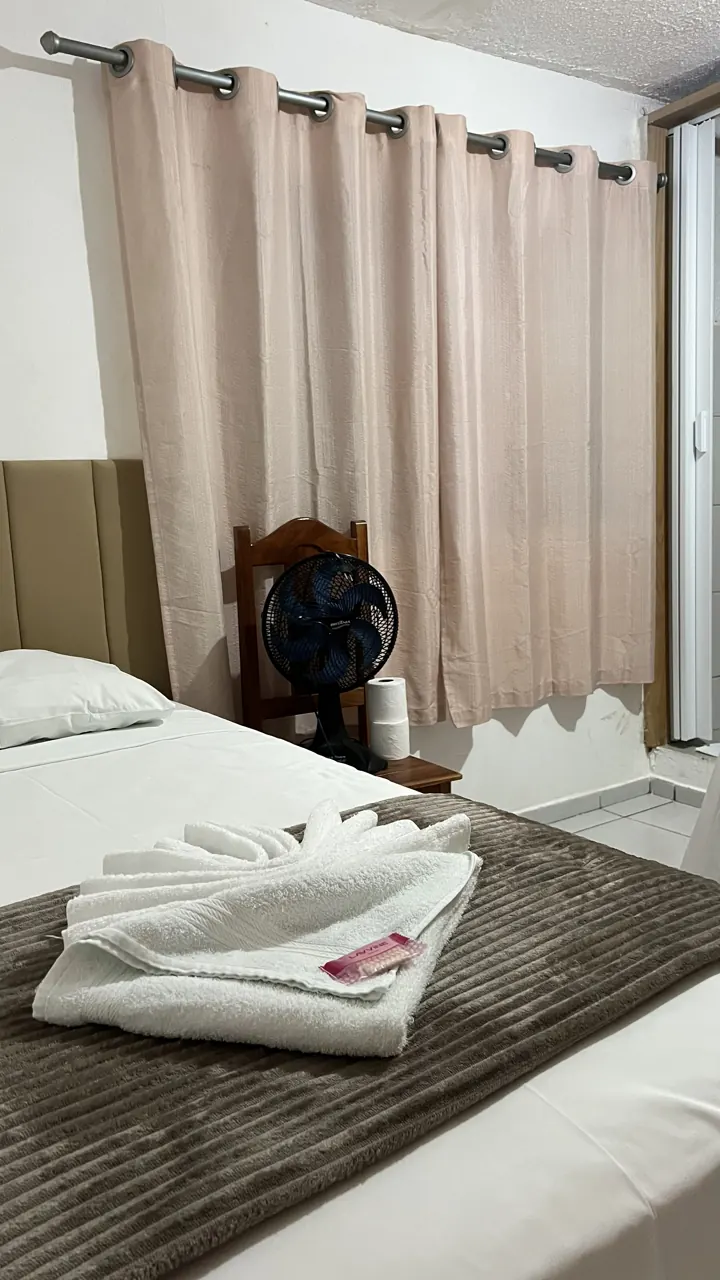 Quarto de casal com cortina clara e toalhas dobradas na cama